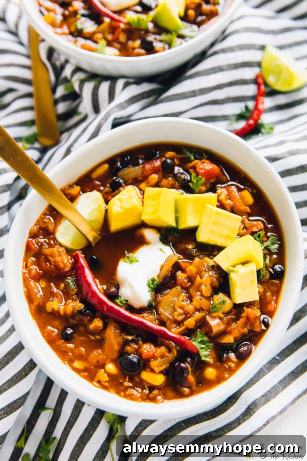 A close-up, top-down view of a bowl of red lentil chili, beautifully garnished with slices of fresh avocado and a dollop of vegan sour cream, highlighting its texture and inviting colors.