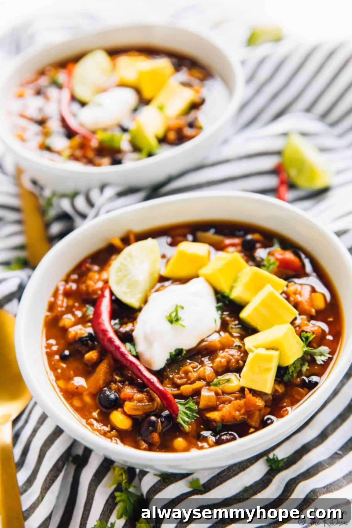 A close-up shot of two white bowls filled with vibrant red lentil chili, resting on a stylish striped cloth, ready to be enjoyed as a comforting meal.
