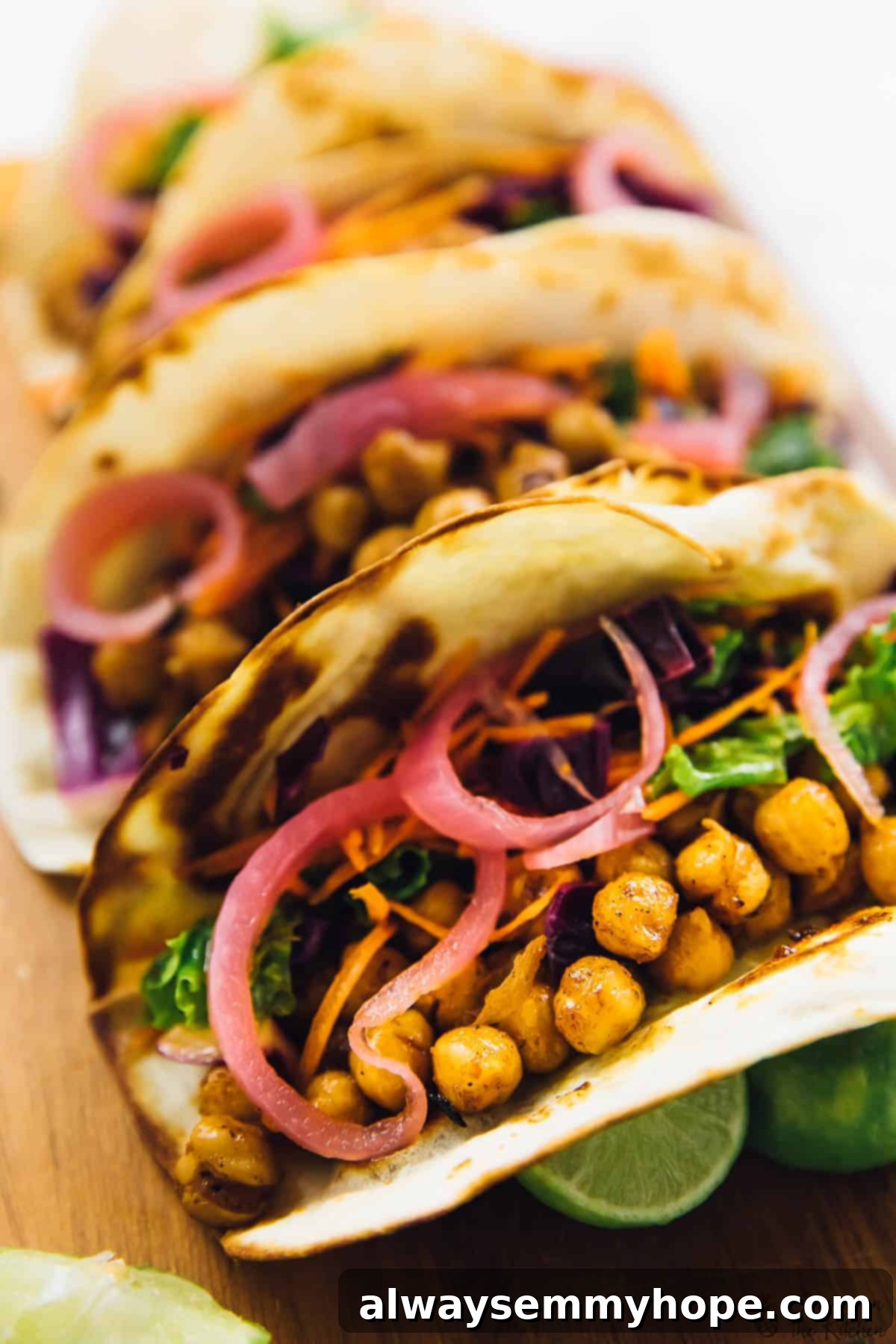 These BBQ chickpea tacos are an easy dinner recipe that comes together in minutes. They're loaded with texture and flavour! Vegan BBQ chickpea tacos arranged on a cutting board, generously topped with vibrant pickled onions and crisp kale slaw.