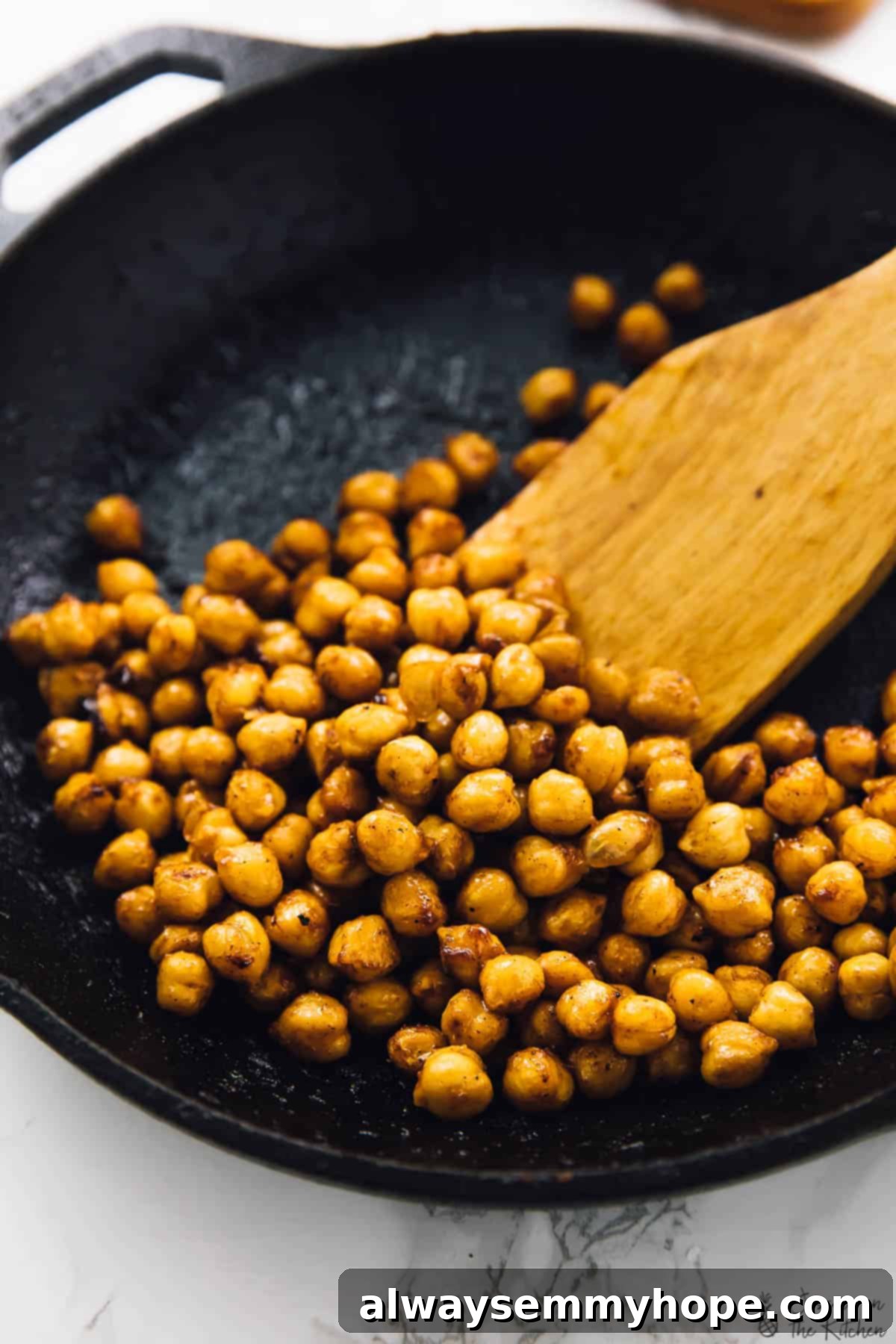 These BBQ chickpea tacos are an easy dinner recipe that comes together in minutes. They're loaded with texture and flavour! BBQ chickpeas simmering in a cast iron skillet with a wooden spatula, ready to be served in tacos.