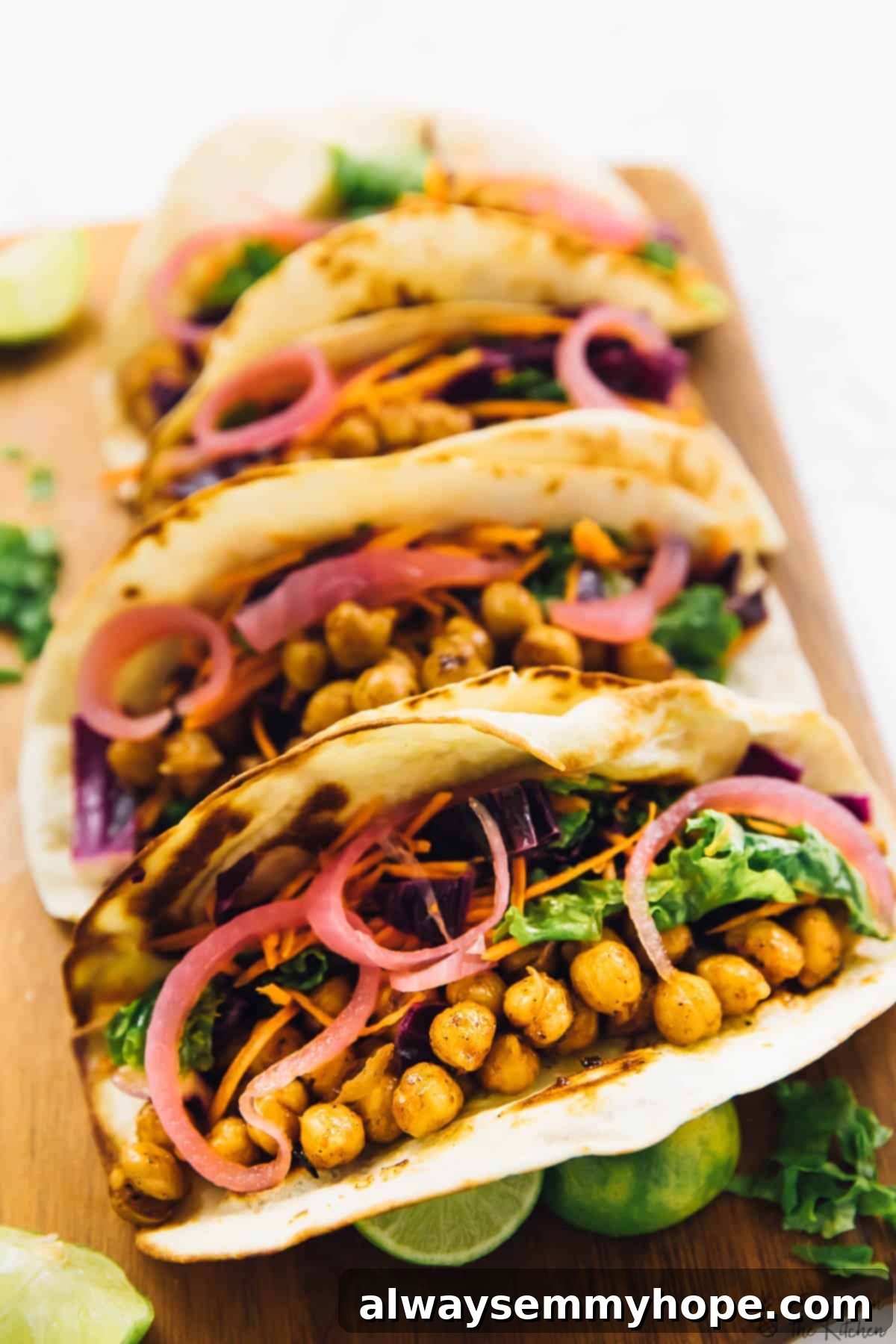 These BBQ chickpea tacos are an easy dinner recipe that comes together in minutes. They're loaded with texture and flavour! Four beautifully assembled vegan BBQ chickpea tacos on a cutting board, garnished with fresh cilantro and lime wedges, topped with pickled onions and slaw.
