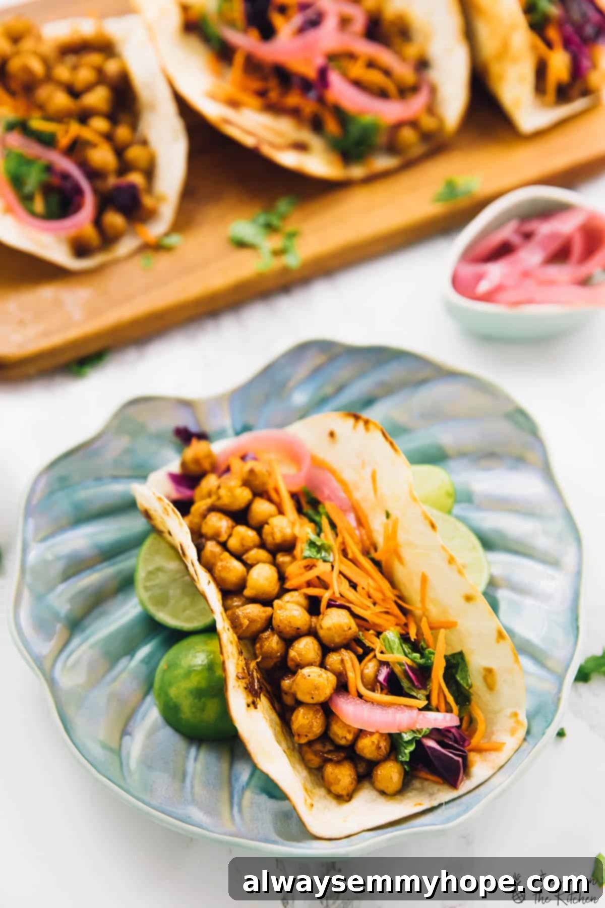 These BBQ chickpea tacos are an easy dinner recipe that comes together in minutes. They're loaded with texture and flavour! A single vegan BBQ chickpea taco on a blue leaf-shaped plate, accompanied by fresh lime wedges, showcasing its vibrant toppings.