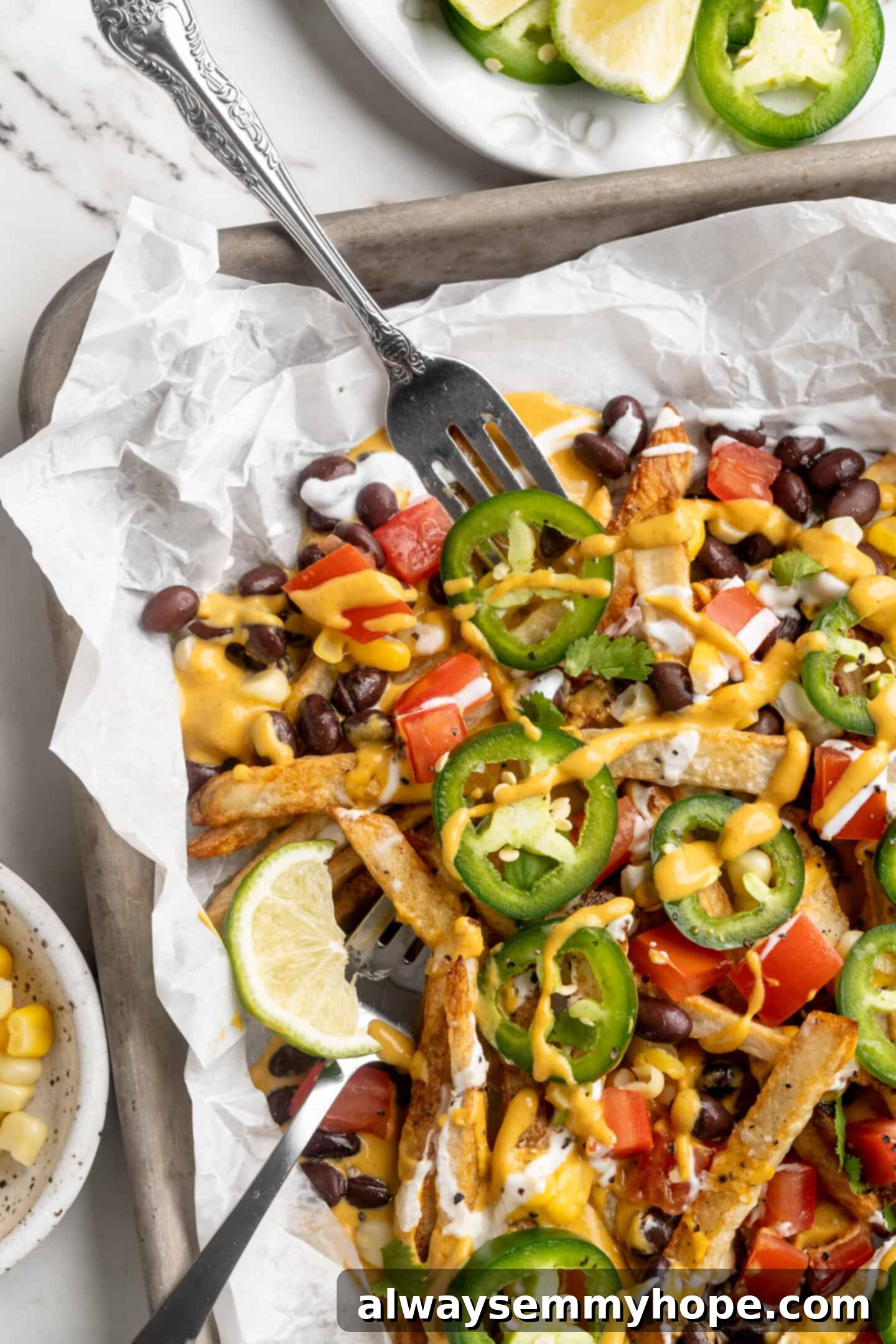 Get the party started with loaded nacho fries! They're topped with all your favourite nacho toppings to create an irresistible appetizer. Sheet pan with loaded nacho fries, with forks digging in, emphasizing the delicious and shareable nature of the dish.