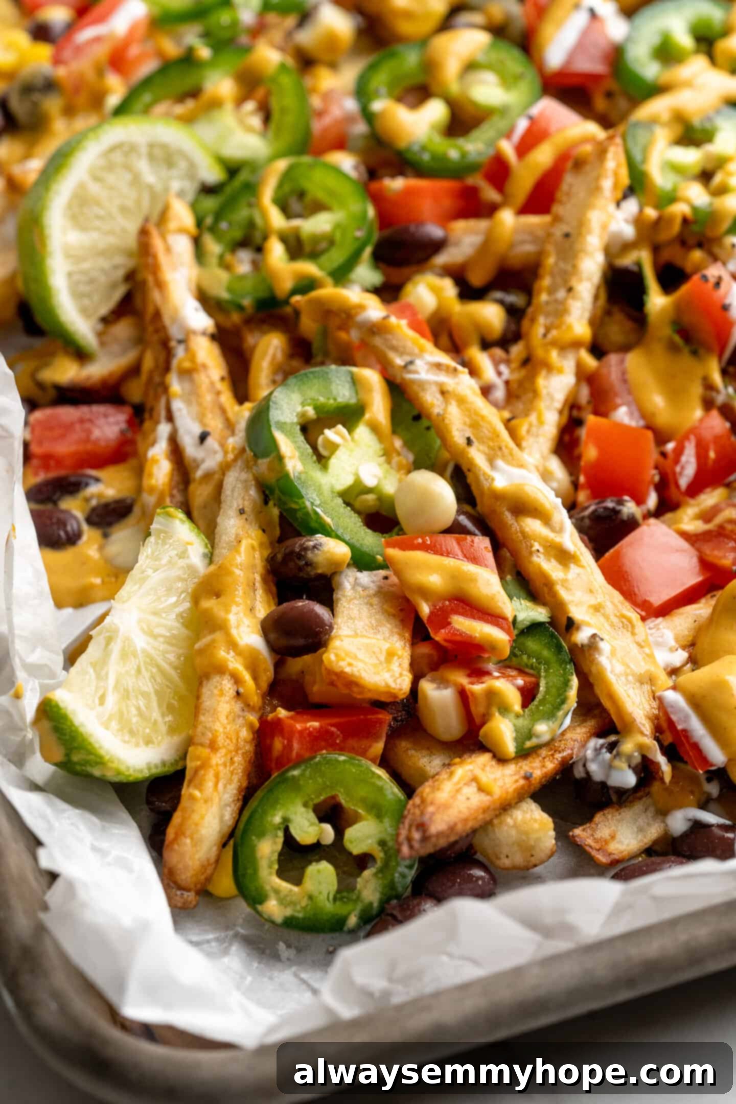 Get the party started with loaded nacho fries! They're topped with all your favourite nacho toppings to create an irresistible appetizer. Loaded nacho fries on a sheet pan, showcasing the crispy texture of the fries and the generous toppings of vegan cheese sauce, beans, corn, and jalapeños.