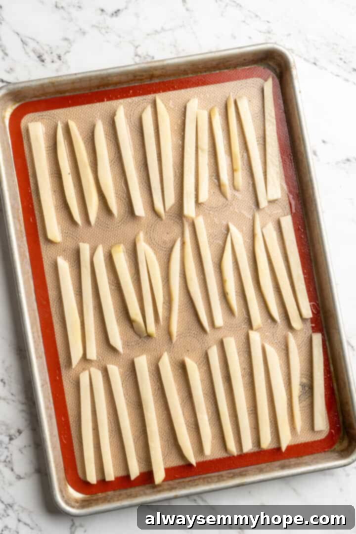 Get the party started with loaded nacho fries! They're topped with all your favourite nacho toppings to create an irresistible appetizer. Overhead view of perfectly cut russet potato sticks arranged on a baking sheet, ready for oiling and baking.