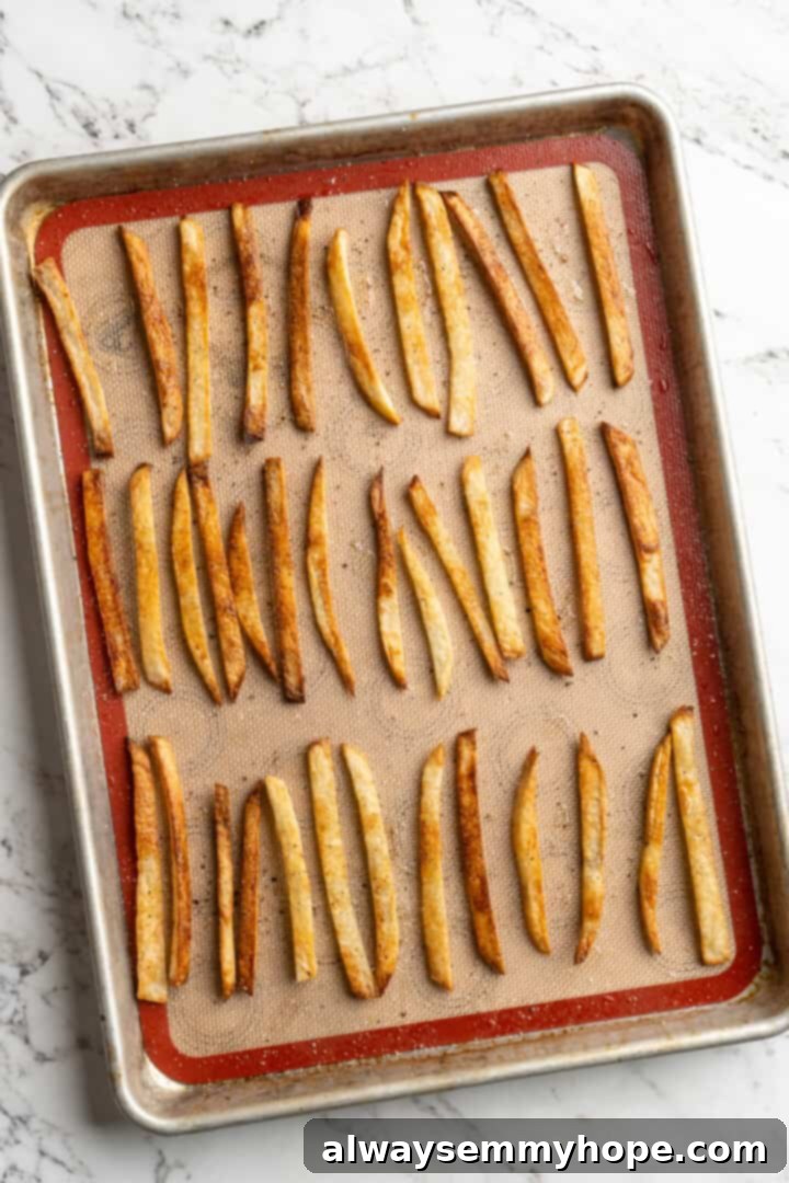 Get the party started with loaded nacho fries! They're topped with all your favourite nacho toppings to create an irresistible appetizer. Overhead view of homemade fries evenly spread out on a baking sheet, coated in oil and ready to be baked until crispy.