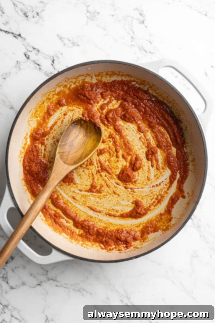This Thai Coconut Curry Soup is creamy, flavourful, and fragrant, with plenty of veggies and noodles to keep you satisfied. Quick and easy! Overhead view of red curry paste and ginger added to sesame oil in pot, stirring to combine.