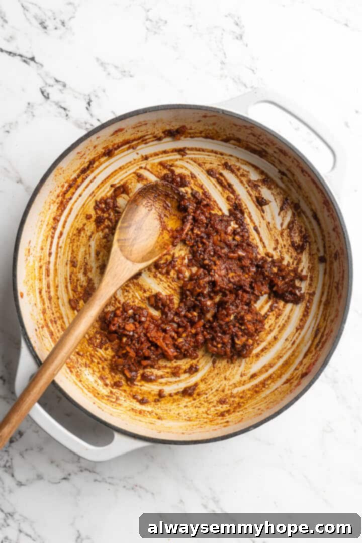 This Thai Coconut Curry Soup is creamy, flavourful, and fragrant, with plenty of veggies and noodles to keep you satisfied. Quick and easy! Overhead view of aromatics including red onion, garlic, ginger, and red curry paste cooking in a pot for soup.