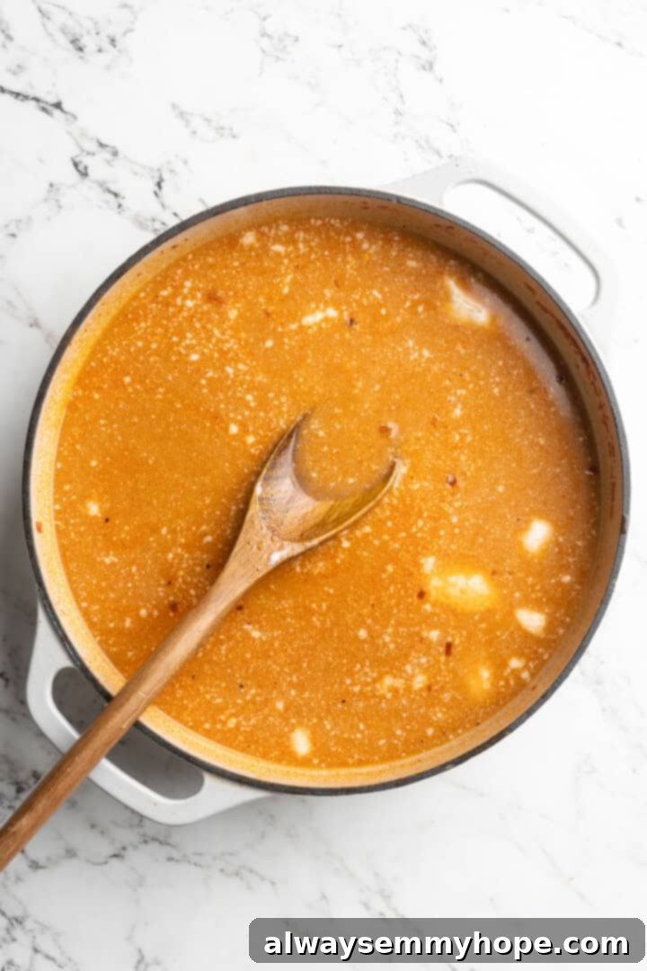 This Thai Coconut Curry Soup is creamy, flavourful, and fragrant, with plenty of veggies and noodles to keep you satisfied. Quick and easy! Overhead view of coconut milk being stirred into the red curry broth base in a pot.