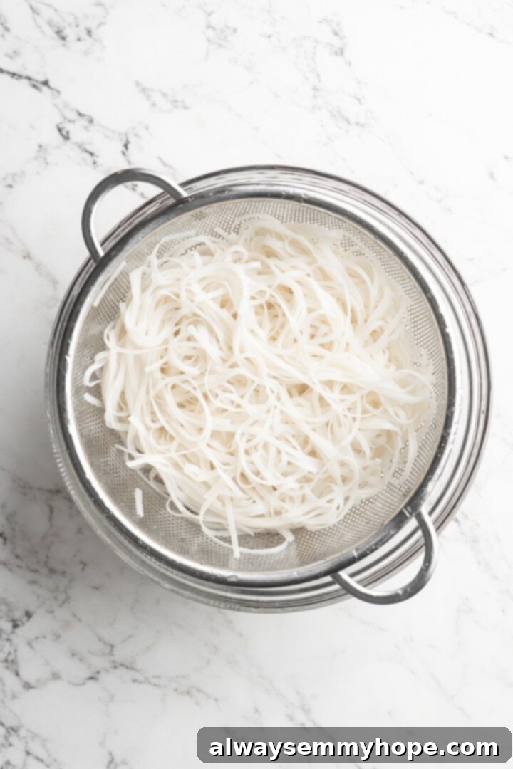 This Thai Coconut Curry Soup is creamy, flavourful, and fragrant, with plenty of veggies and noodles to keep you satisfied. Quick and easy! Overhead view of cooked rice noodles in a colander, ready to be added to soup.