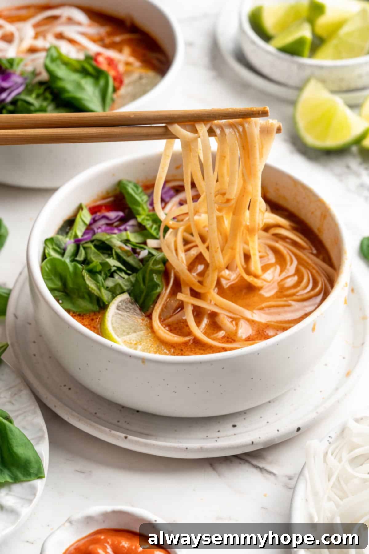 This Thai Coconut Curry Soup is creamy, flavourful, and fragrant, with plenty of veggies and noodles to keep you satisfied. Quick and easy! Thai coconut curry soup with noodles in a white bowl, garnished with fresh basil leaves and a lime wedge.