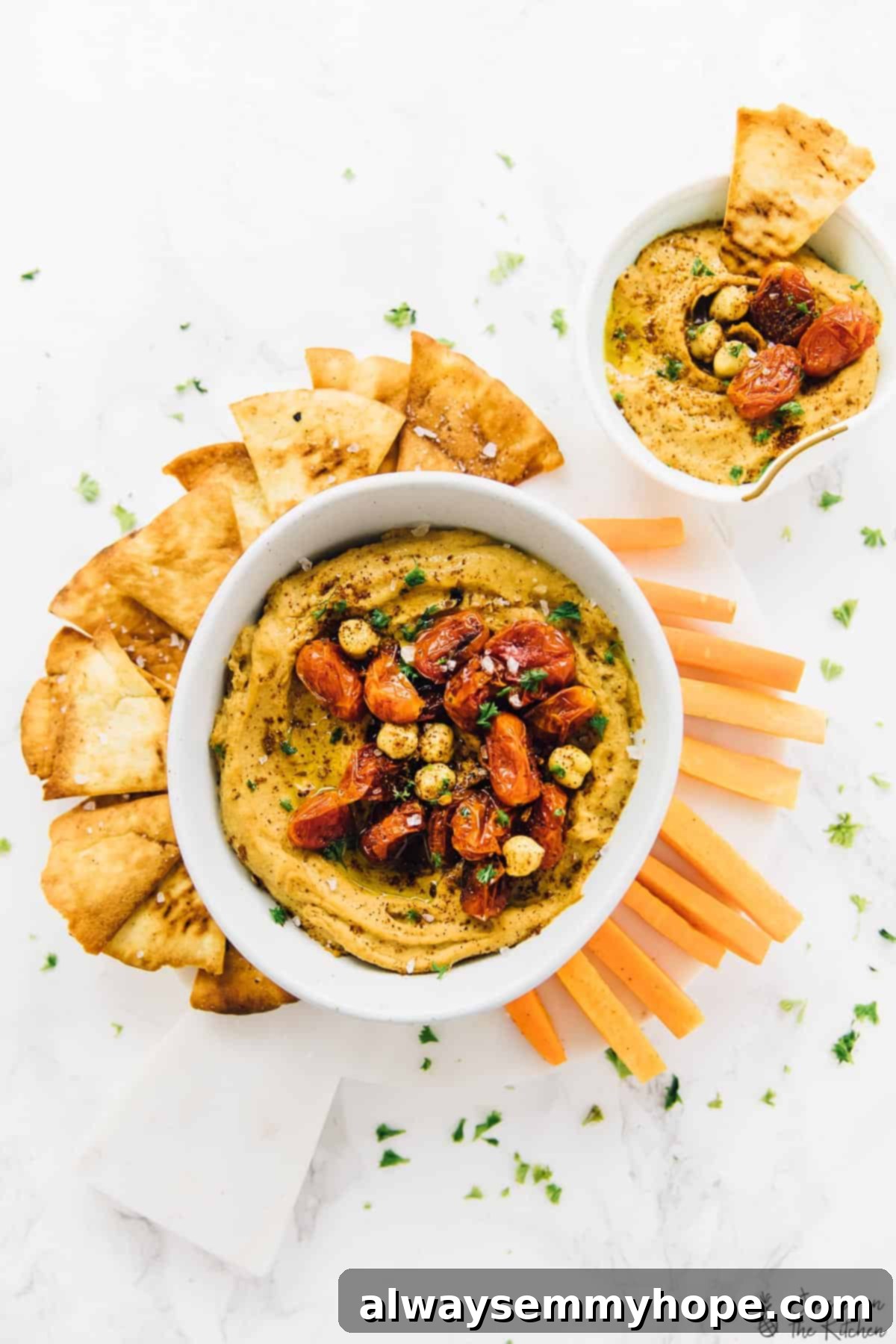 This roasted red pepper hummus recipe is sweet, savoury, smoky, and spicy. It's easy to make and ready to impress! Overhead view of two bowls of roasted red pepper hummus with carrot sticks and pita chips