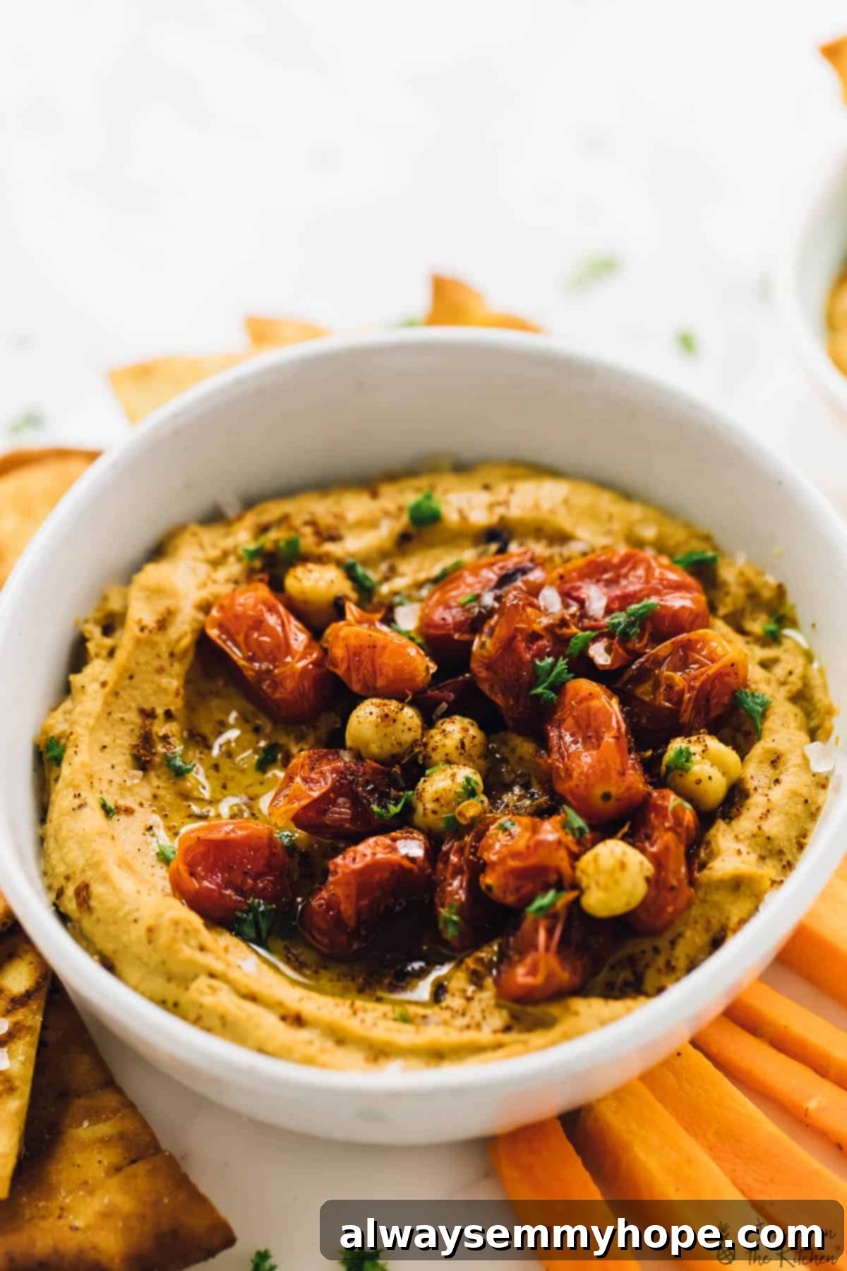 This roasted red pepper hummus recipe is sweet, savoury, smoky, and spicy. It's easy to make and ready to impress! Bowl of roasted red pepper hummus with roasted cherry tomatoes and chickpeas for garnish