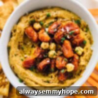 Fire-Roasted Red Pepper Hummus 2 Overhead view of spicy roasted red pepper hummus in a white bowl with carrots and toasted pita chips on the side.