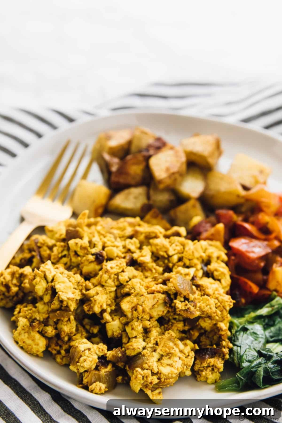 Close up shot of Southwestern tofu scramble on a plate, garnished with fresh herbs and served with a side of breakfast potatoes and vegetables.
