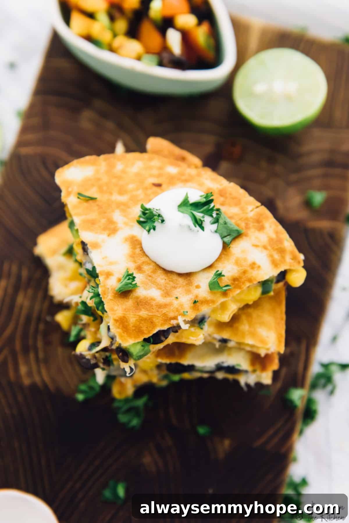 These easy black bean and corn quesadillas are done in just 15 minutes, making them perfect for a quick weeknight dinner! A stack of golden-brown black bean and corn quesadilla wedges, garnished with fresh herbs, resting on a wooden board.