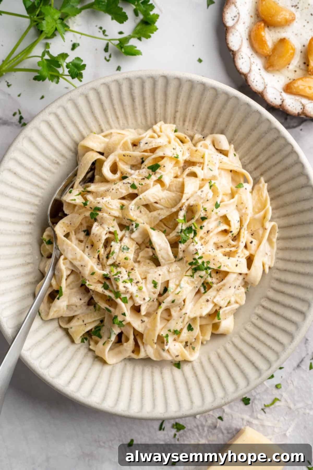 Overhead view of vegan garlic Alfredo pasta in bowl with spoon, garnished with fresh parsley.
