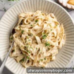 Overhead view of vegan garlic Alfredo pasta in bowl with spoon, garnished with fresh parsley.