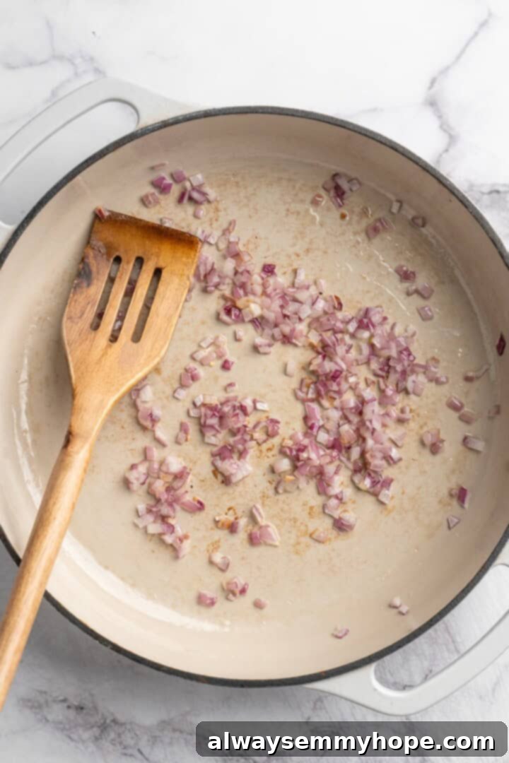 Overhead view of finely minced red onions gently cooking in a skillet until translucent.