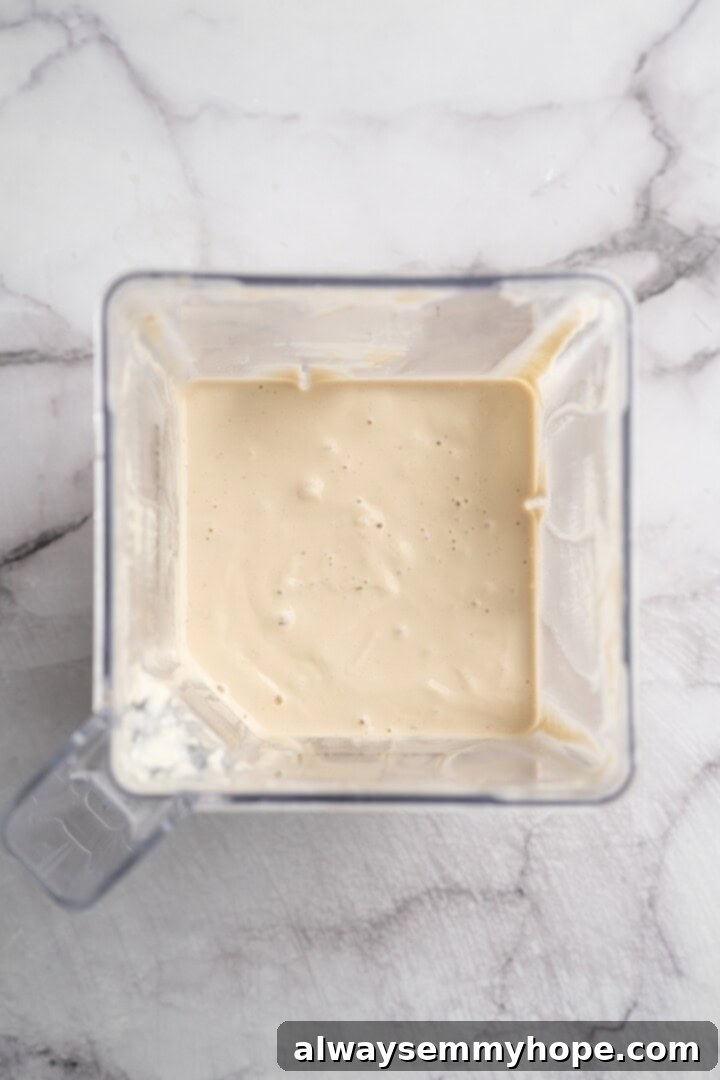 Overhead view of all Alfredo sauce ingredients blending to a smooth consistency in a high-speed blender.