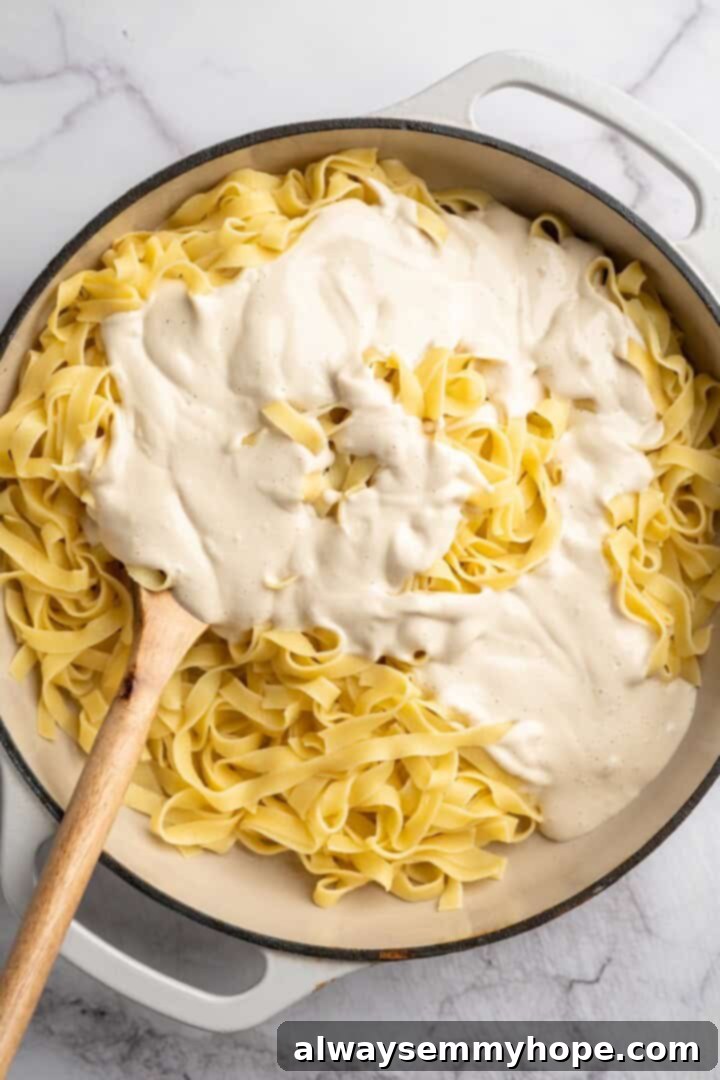 Overhead view of freshly blended vegan Alfredo sauce being poured over cooked fettuccine in a skillet.