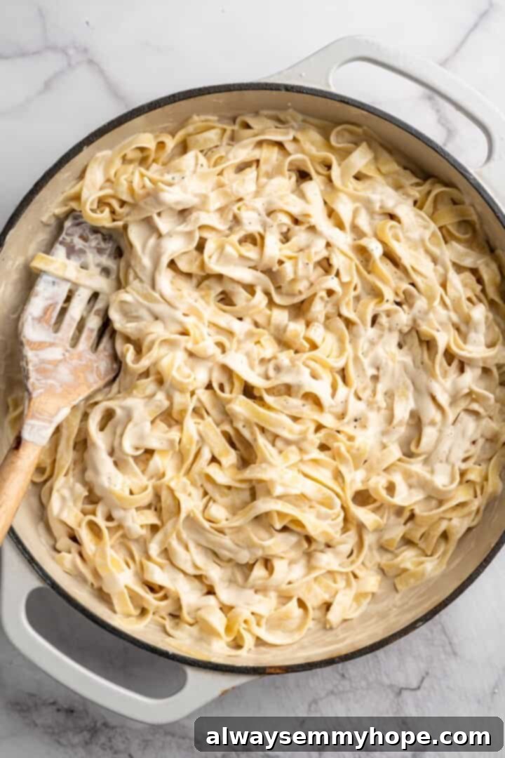 Overhead view of vegan garlic Alfredo pasta being tossed in a skillet, thoroughly coated in sauce.