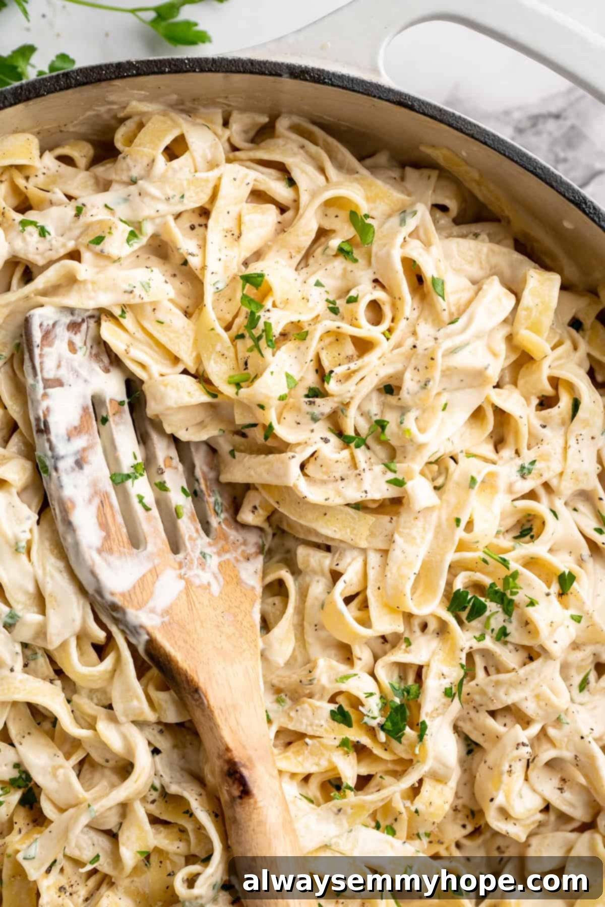 Close-up of vegan garlic Alfredo pasta in a skillet, ready to be served, with a wooden spoon.