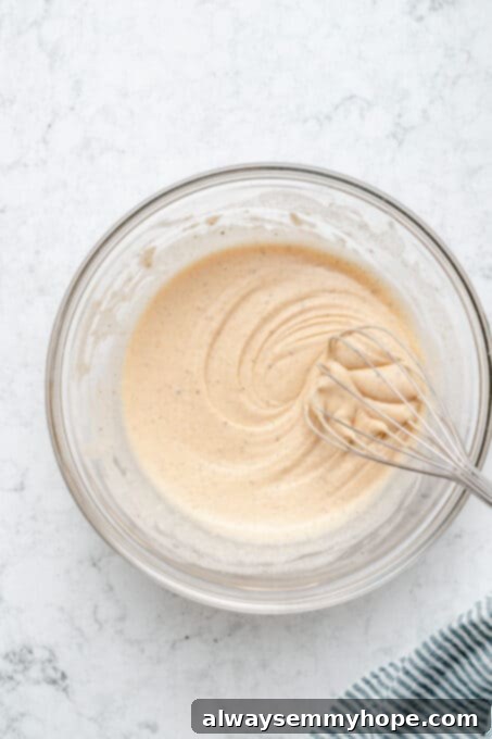 Smooth beer batter in a glass bowl with a whisk, ready for coating.