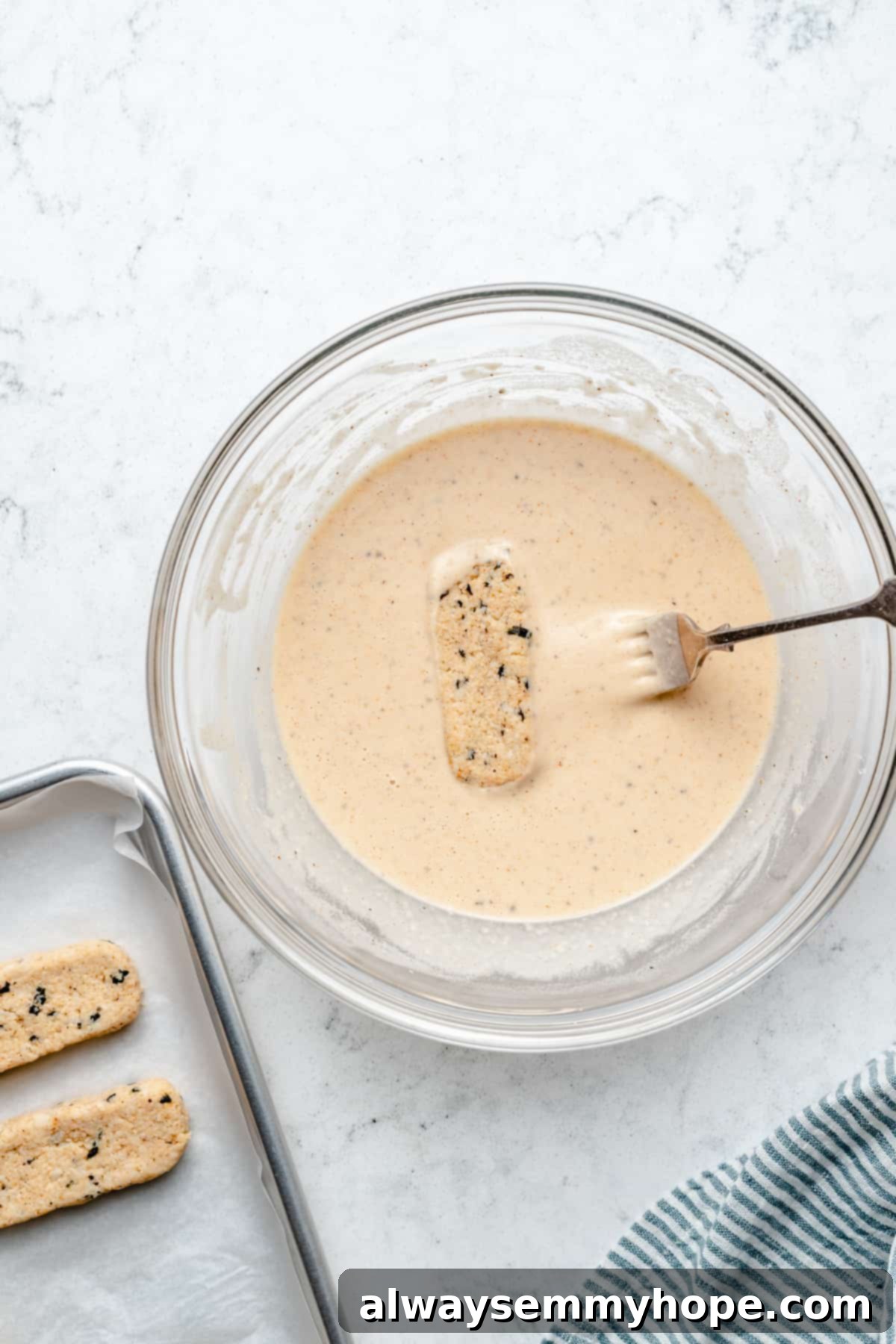 Overhead view of a vegan fish stick being generously coated in the beer batter.