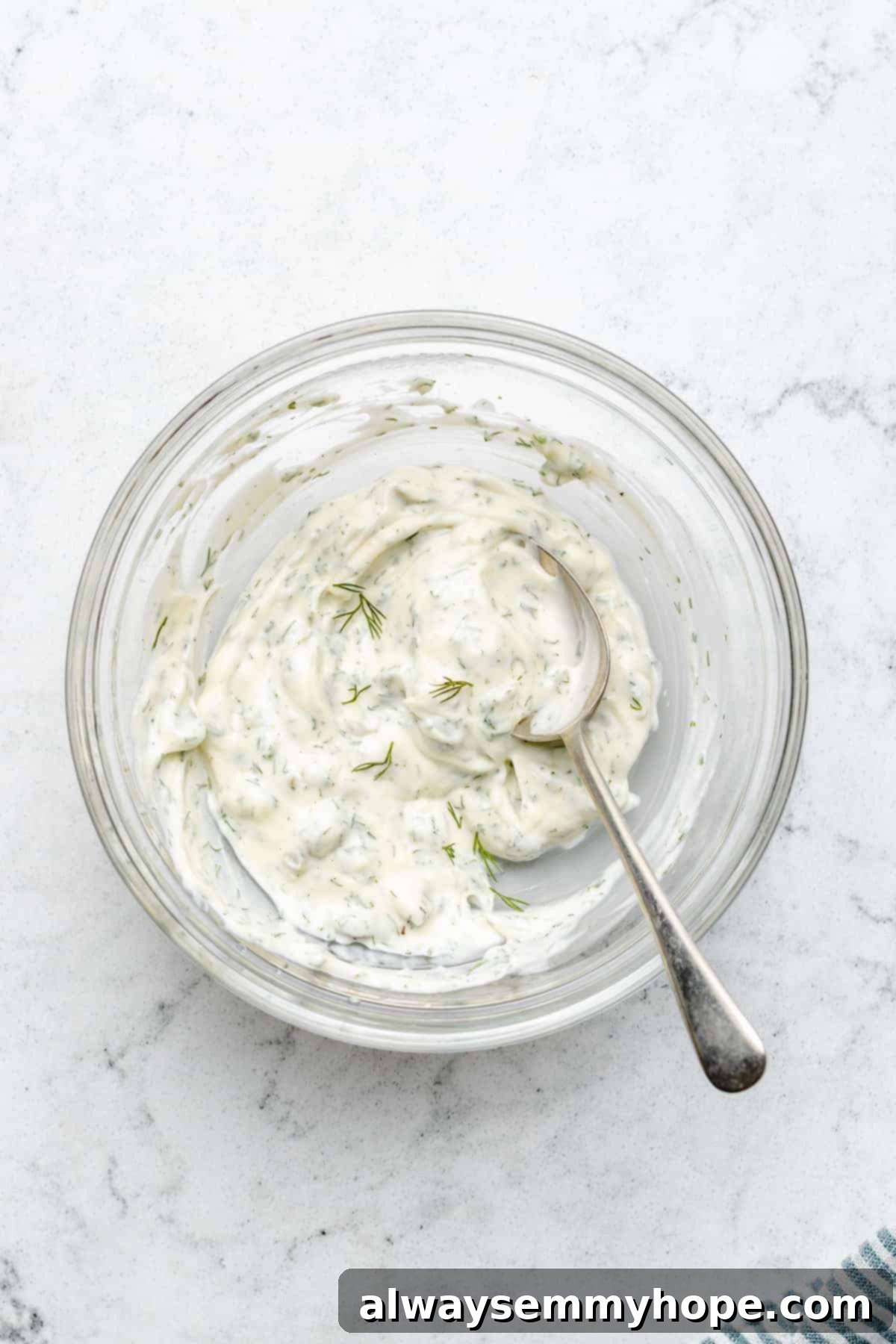 Overhead view of creamy vegan tartar sauce in a glass bowl with a spoon, ready for dipping.
