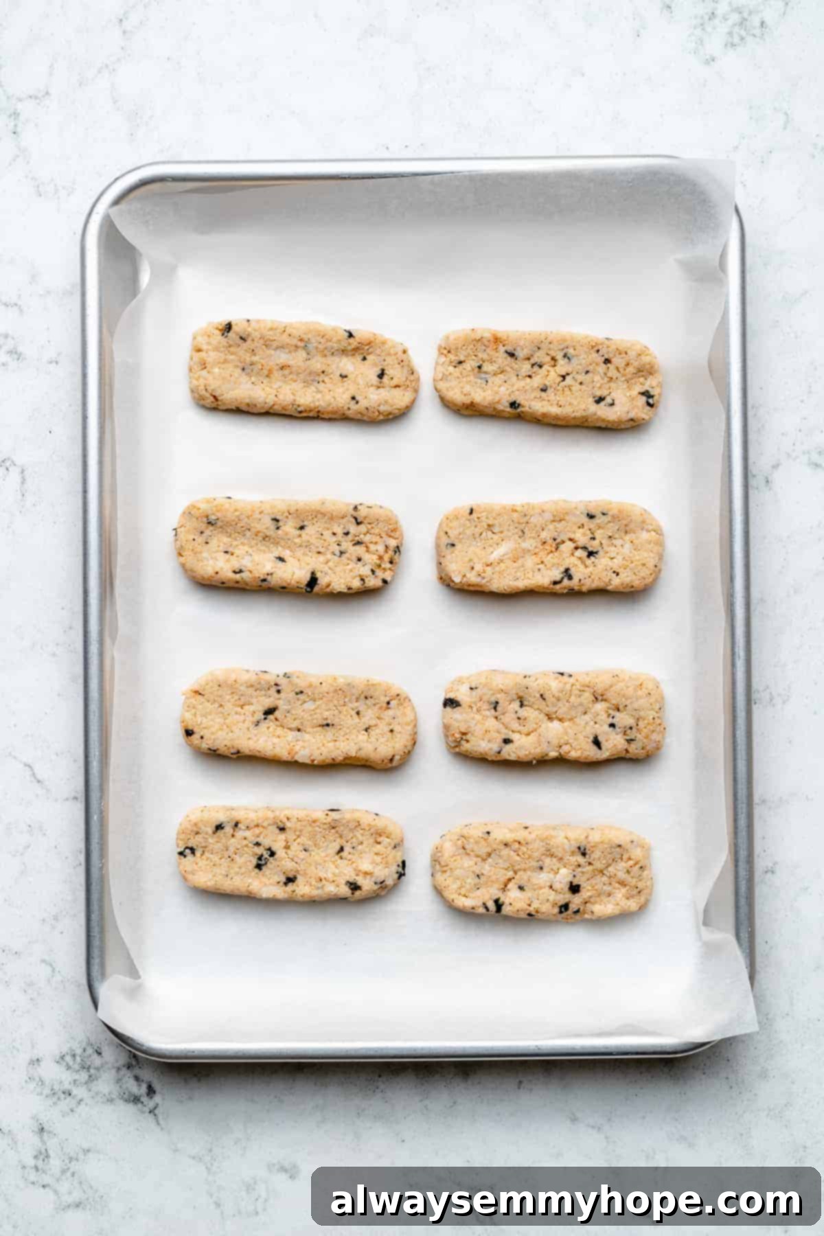 Overhead view of shaped vegan fish sticks neatly arranged on a parchment-lined baking sheet.