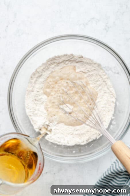 Overhead view of beer being poured into a glass bowl containing dry batter ingredients.