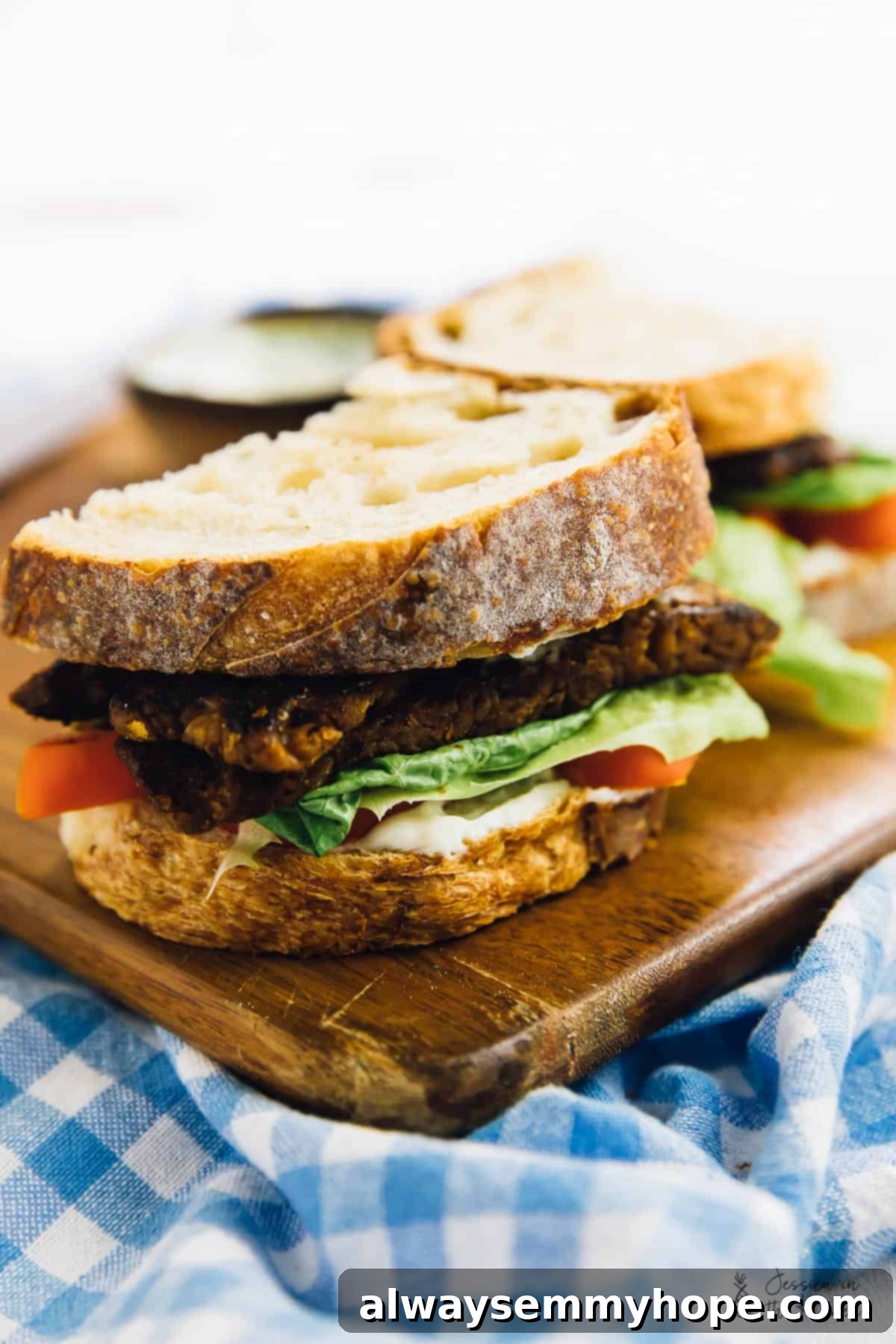 Vegan BLT sandwich sliced in half, showcasing the layers of tempeh bacon, crisp lettuce, and juicy tomato.