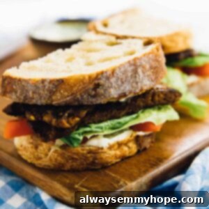 A vegan BLT, cut in half, on a wood board, with tempeh bacon visible.