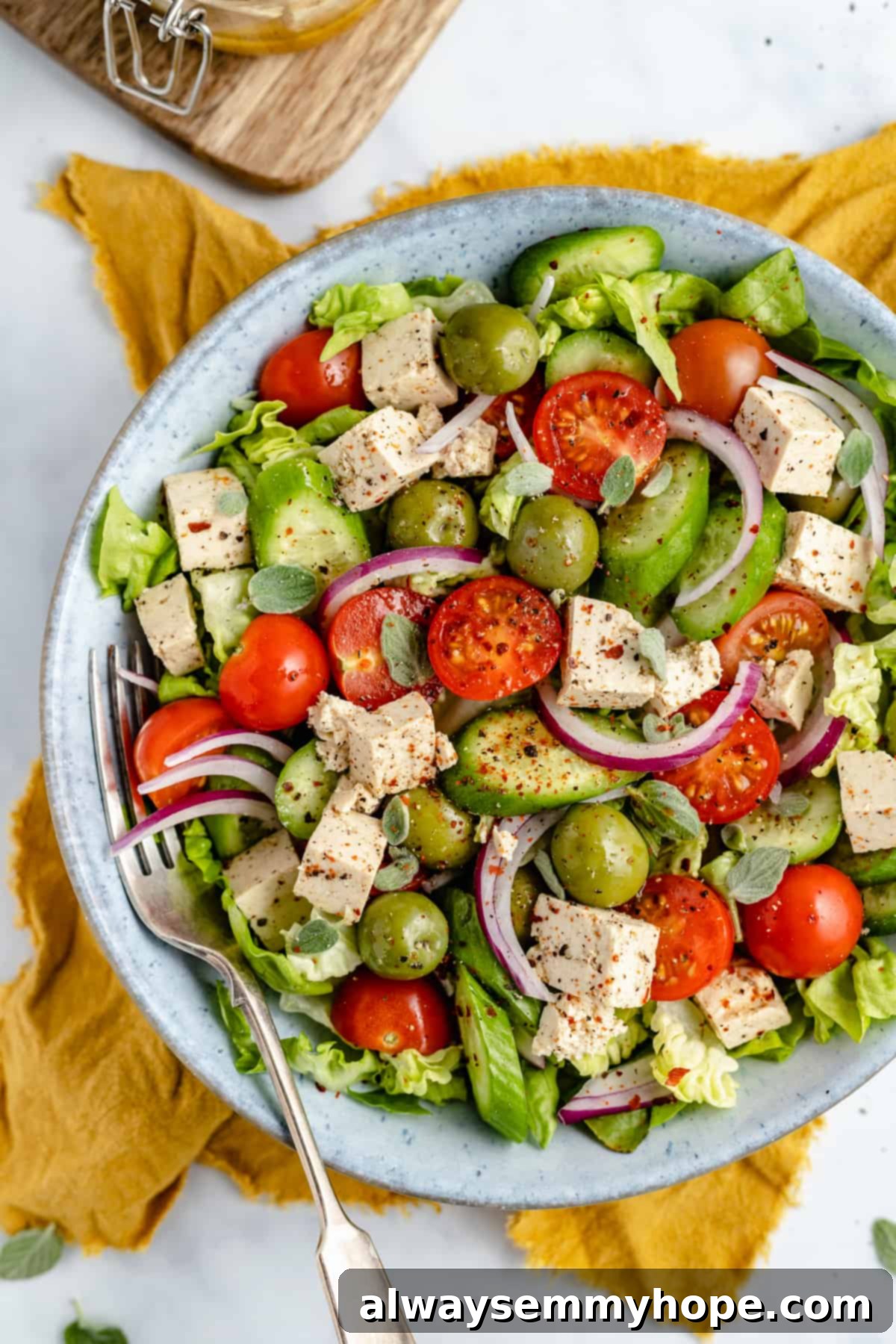 Vegan tofu feta cheese is a quick and easy plant-based substitute that needs only 6 ingredients. Enjoy it on salads, sandwiches, and more! vegan feta cheese salad in a blue bowl on a yellow napkin