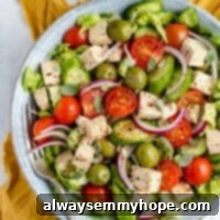 Vegan Tofu Feta 2 Overhead view of a fresh green salad topped with vegan feta cheese cubes in a blue bowl, with more tofu feta cheese in a jar in the background.