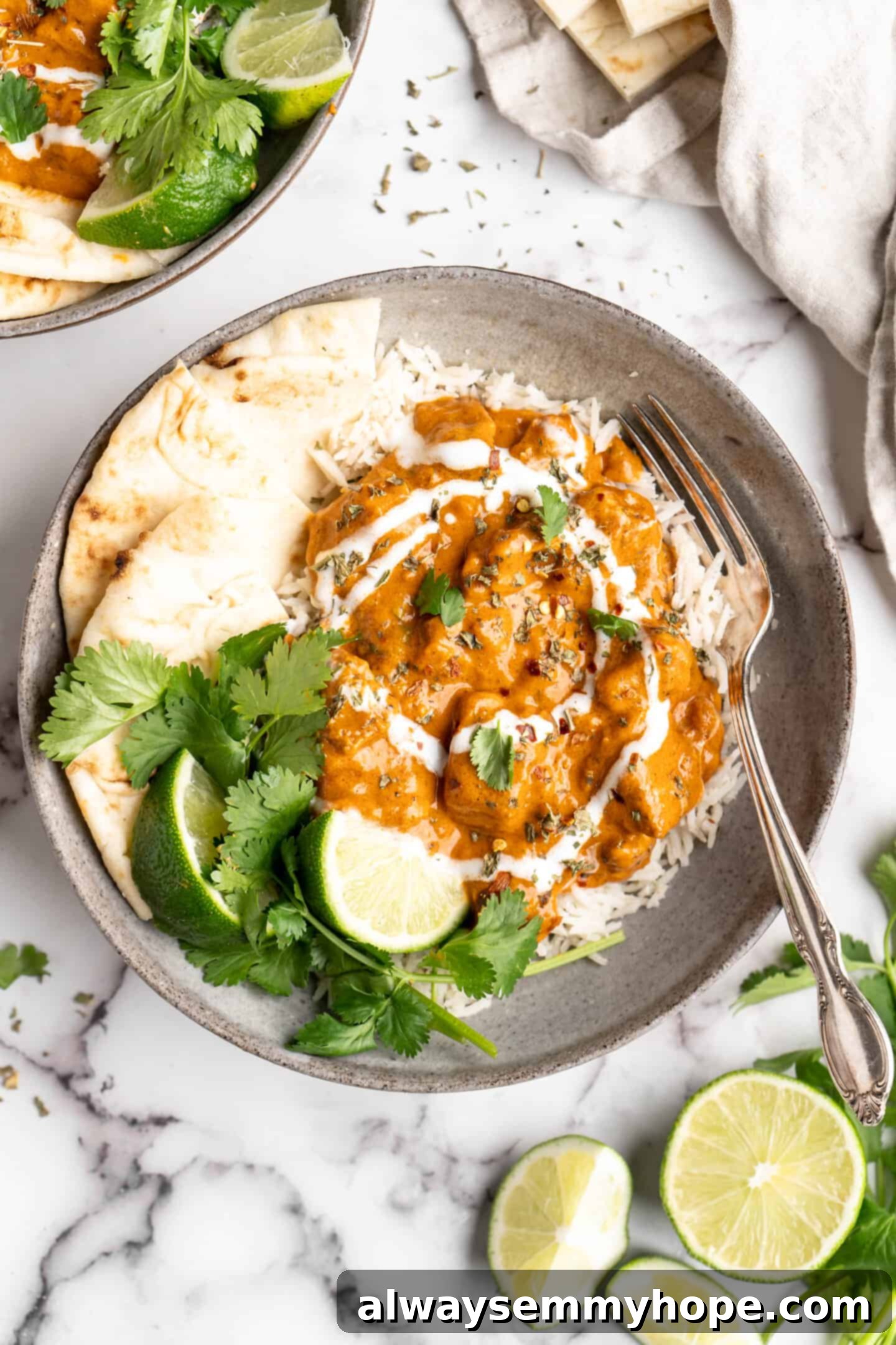 Vegan butter chicken in bowl with rice, naan, and garnishes, showcasing a rich and creamy sauce with golden tofu
