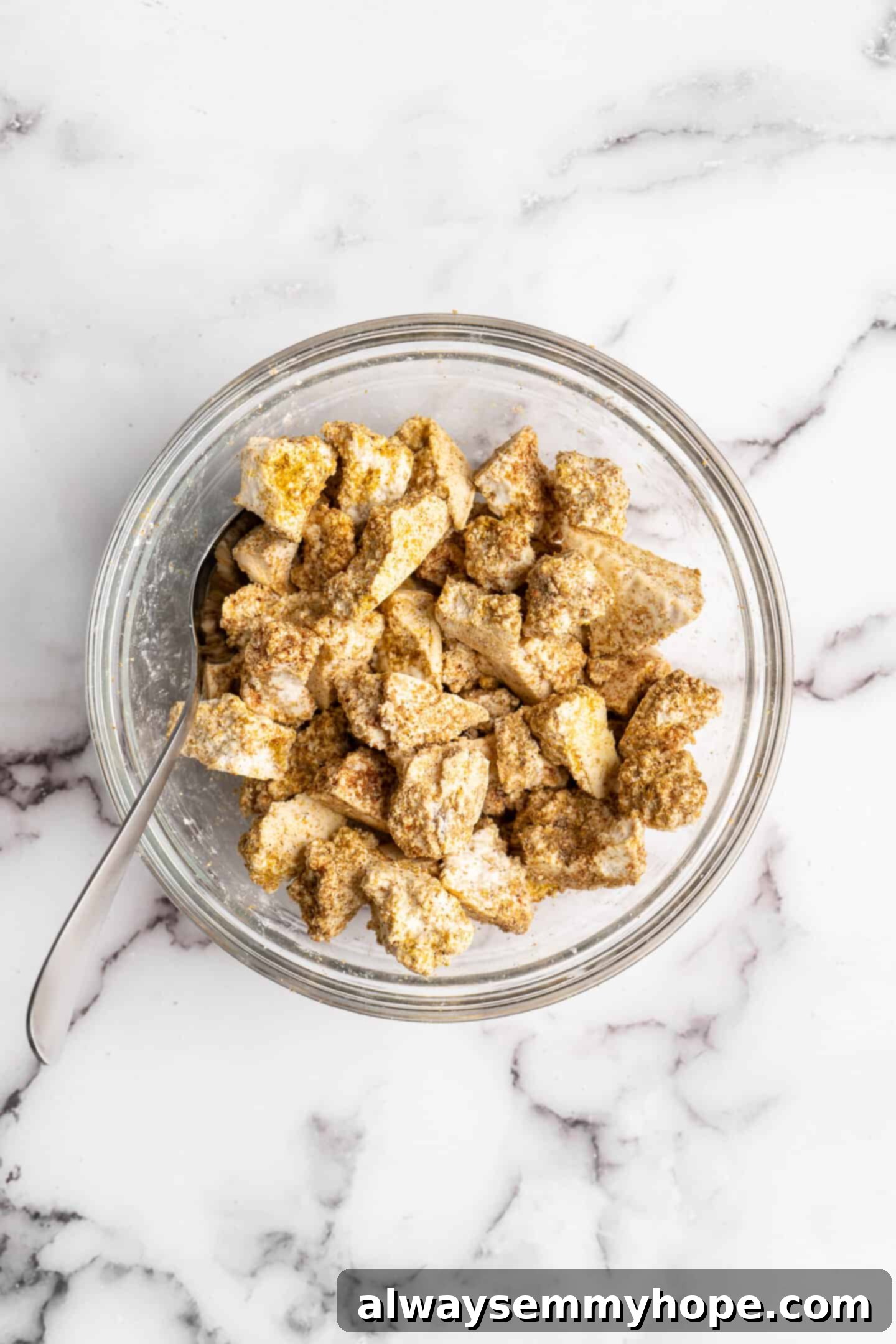 Overhead view of tofu cubes evenly tossed with cornstarch and spices in a large bowl, ready for cooking