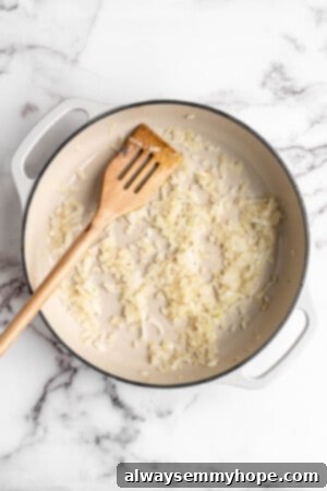 Overhead view of diced onions sautéing until translucent in a Dutch oven, forming the aromatic base of the sauce