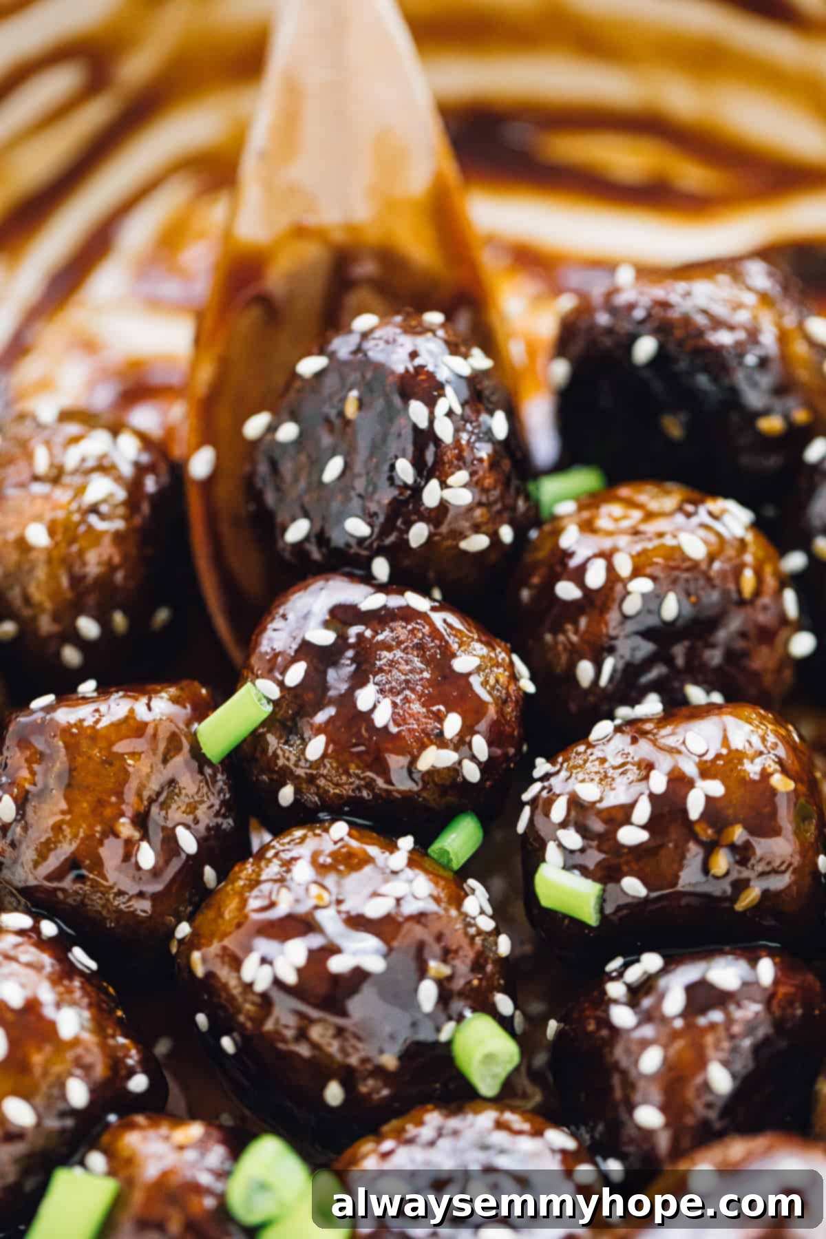 Vegan teriyaki meatballs are easy to make, slathered with flavor-packed homemade teriyaki sauce. Great for dinner, appetizers, or meal prep! A wooden spoon stirring a pan of saucy vegan meatballs garnished with sesame seeds and scallions