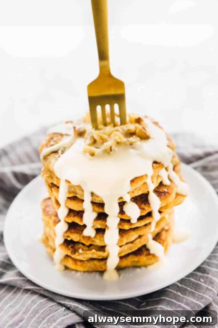 A stack of fluffy vegan carrot cake pancakes, drizzled with a rich maple cream cheese frosting.