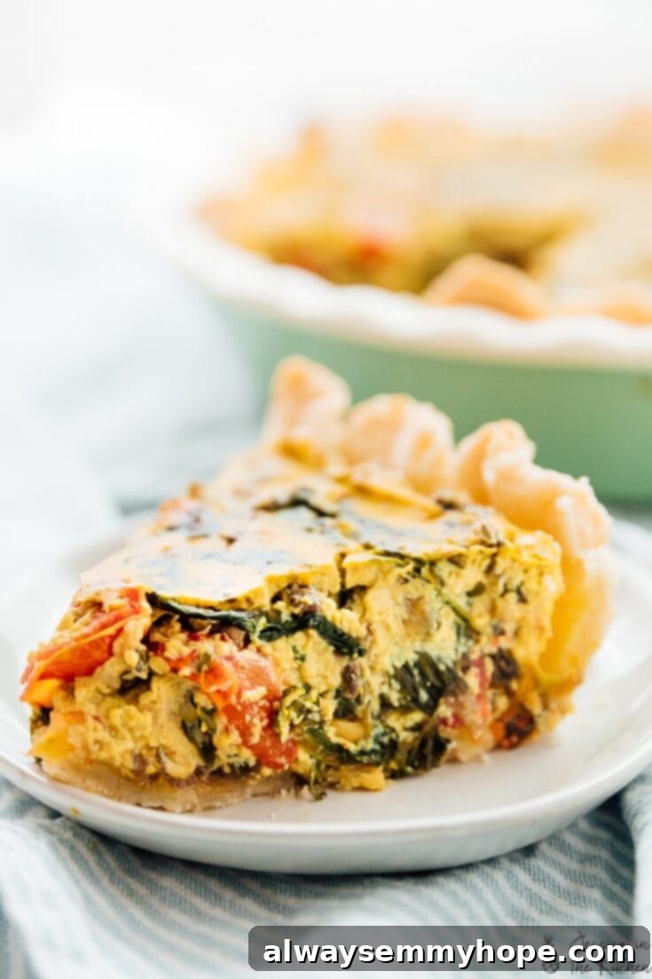 A slice of savory vegan quiche, brimming with colorful vegetables like tomatoes, spinach, and mushrooms.