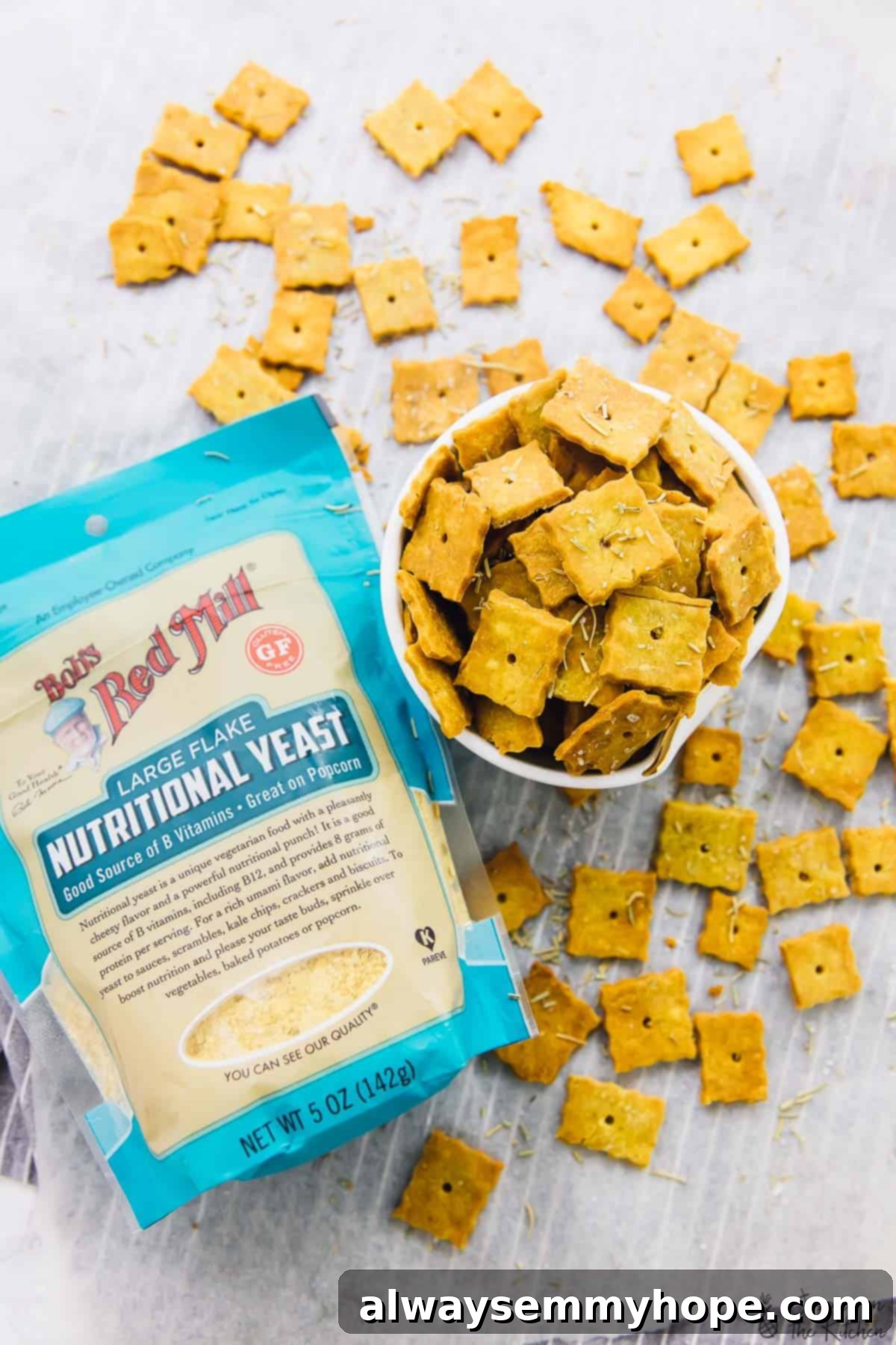 Overhead view of vegan herbed parmesan crackers in a bowl with a pack of nutritional yeast next to it. 