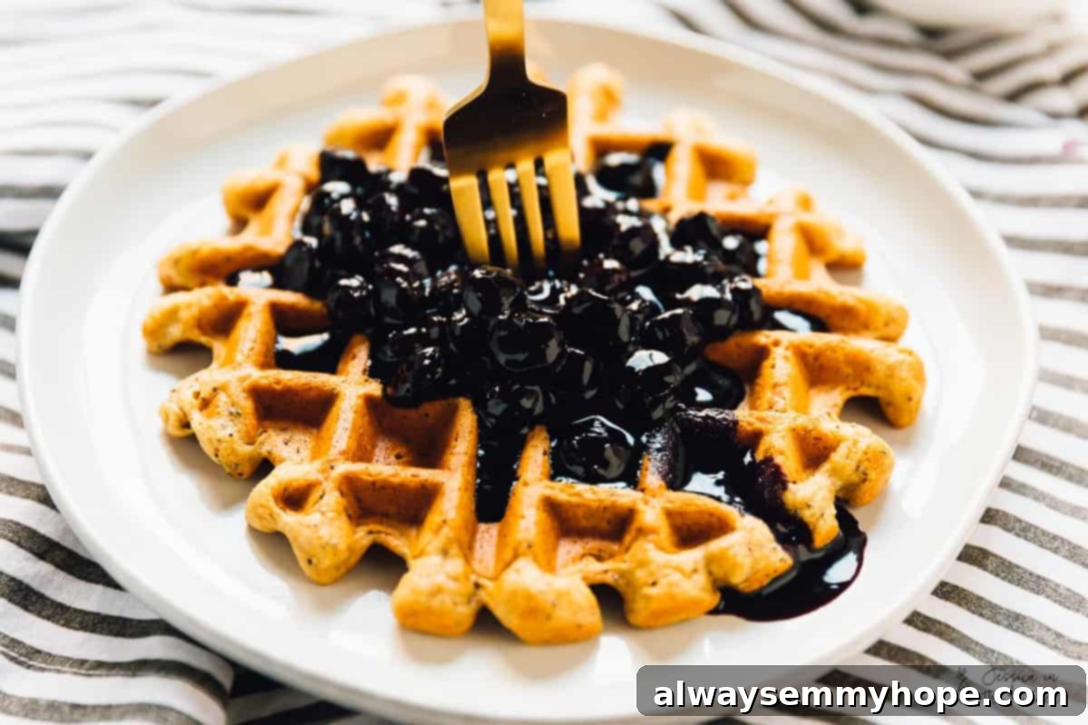 A gold fork delicately holding a portion of lemon poppyseed waffle, showcasing its texture and the blueberry sauce.