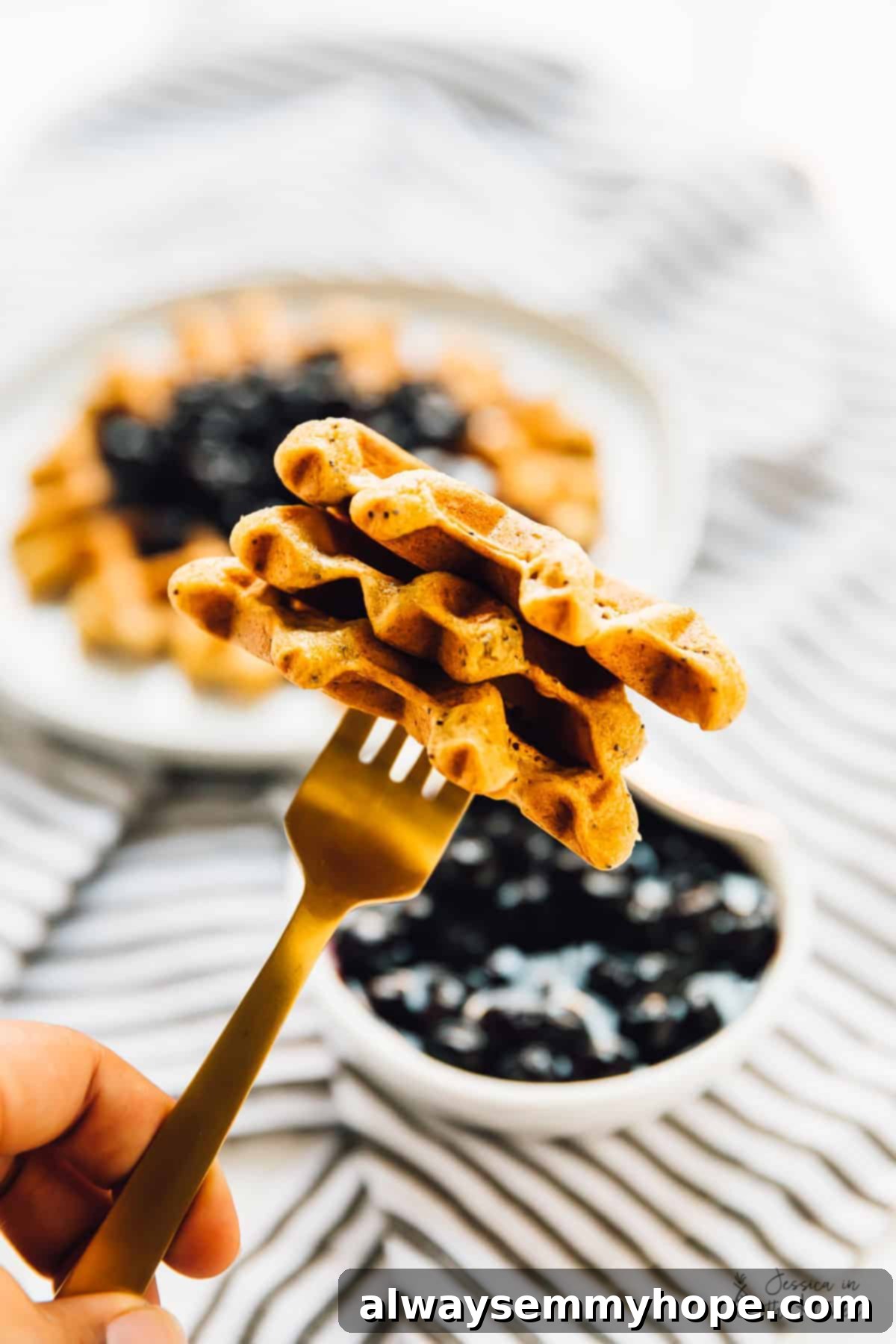 A close-up shot of a perfect bite of lemon poppyseed waffle on a gold fork, covered in blueberry sauce.