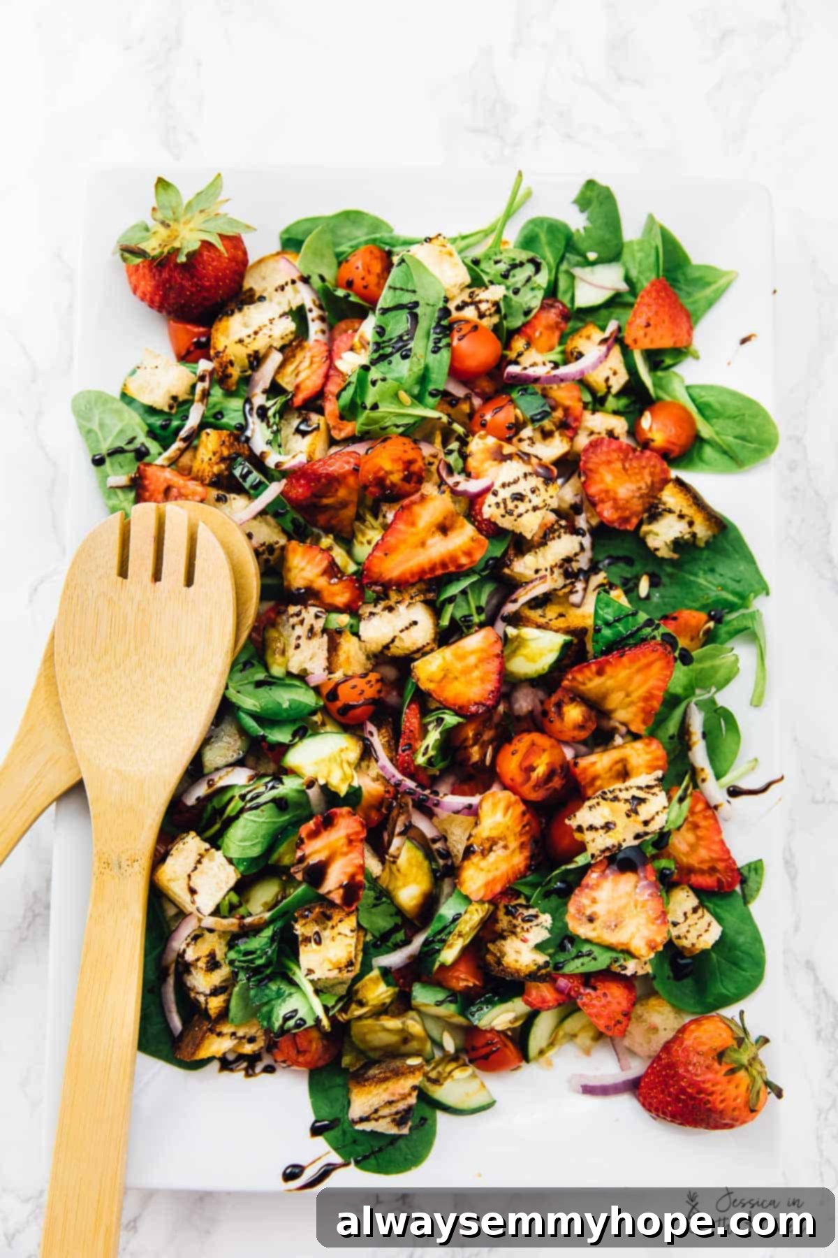 Top down view of strawberry panzanella salad with a wooden spork on the side, highlighting its vibrant colors and fresh ingredients.