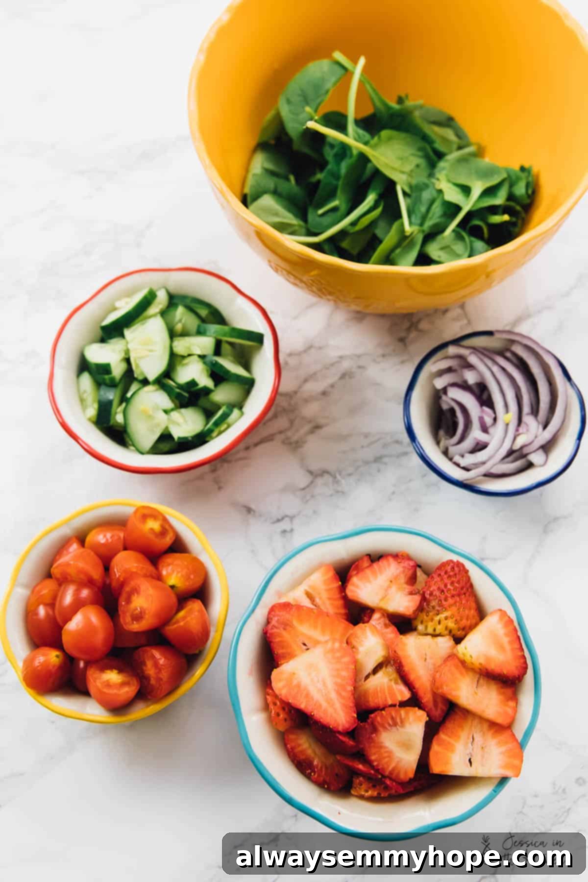 Top down view of finely chopped strawberries, ripe cherry tomatoes, crisp cucumbers, thinly sliced red onions, and fresh spinach, ready to be combined for a delicious salad.