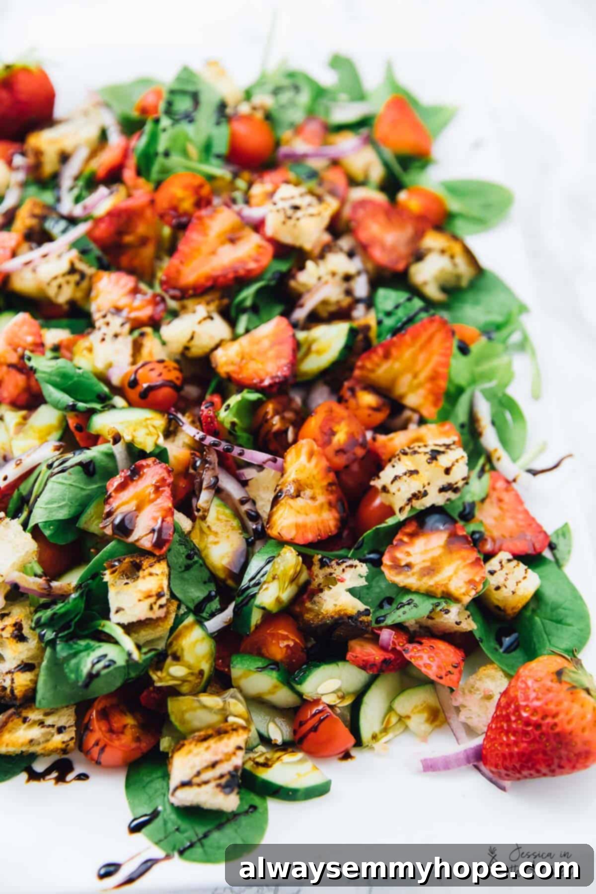 Strawberry Panzanella Salad elegantly drizzled with a rich balsamic glaze, enhancing its visual appeal and flavor profile.