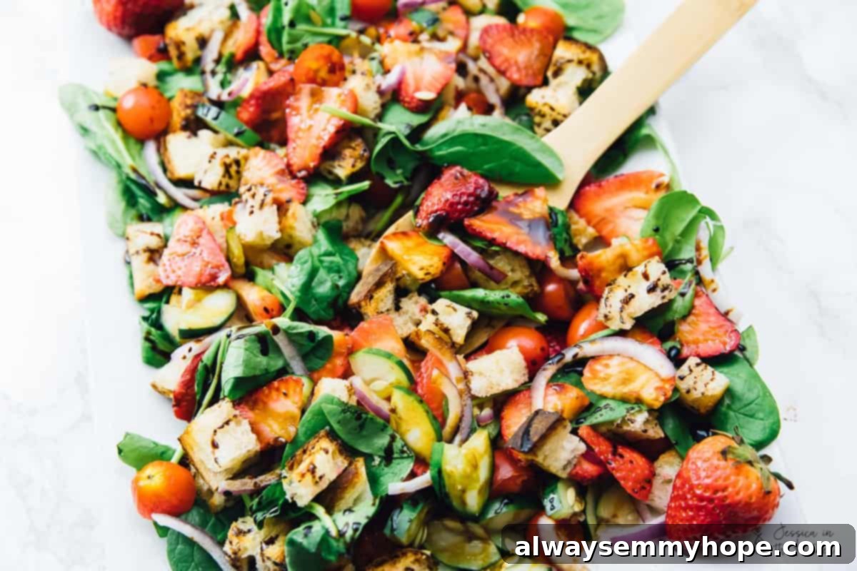 A wooden spoon poised within a bowl of Strawberry Panzanella Salad, ready to serve a delicious portion.