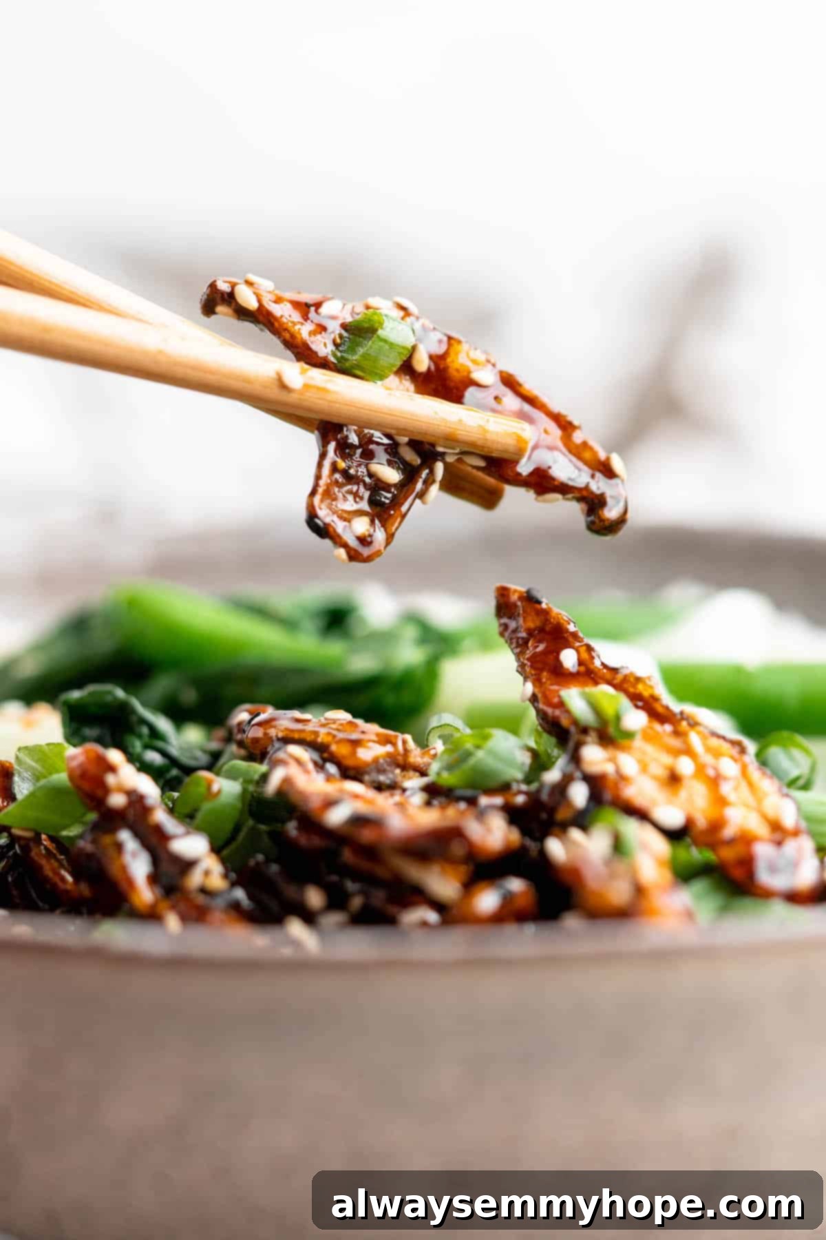 Closeup of sticky sesame shiitake mushroom being picked up with chopstick